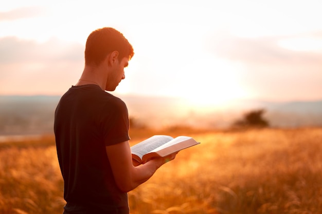 Mens bidden op de Heilige Bijbel in een veld tijdens prachtige zonsondergang.