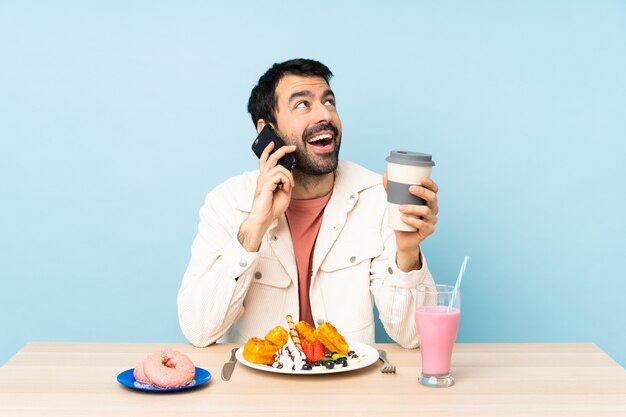 Mens bij een lijst die ontbijtwafels heeft en een milkshake holdingskoffie en mobiel meenemen