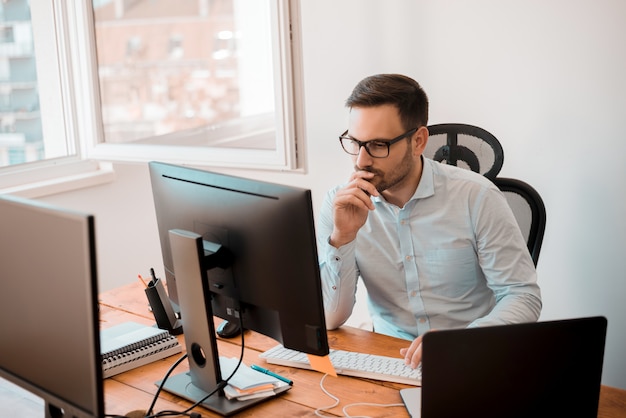 Mens die aan computer in modern bureaubinnenland werkt.