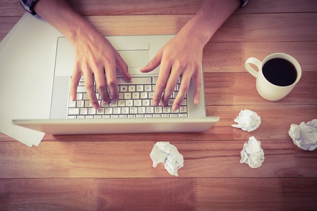 Mens die aan laptop door zwarte koffie bij bureau in bureau werkt