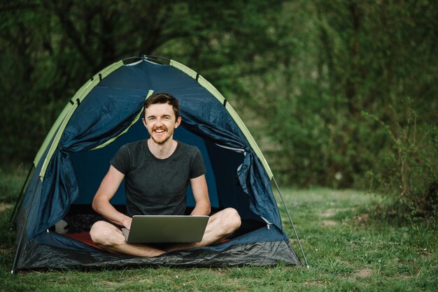 Mens die aan laptop in tent in aard werkt