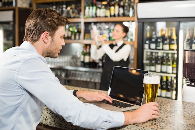 Mens die aan laptop met in hand bier werkt