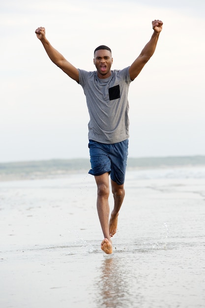 Foto mens die blootvoets op strand met wapens loopt die in overwinning worden opgeheven