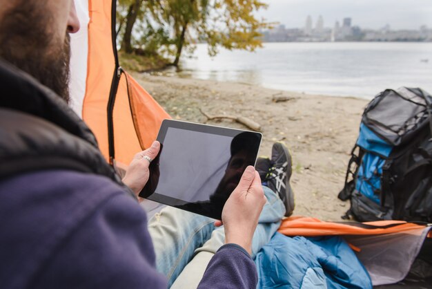 Mens die digitale tablet in het kamperen tent gebruiken