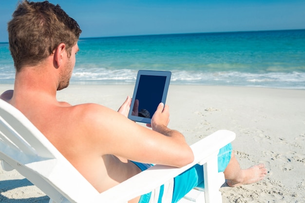 Mens die digitale tablet op ligstoel gebruiken bij het strand