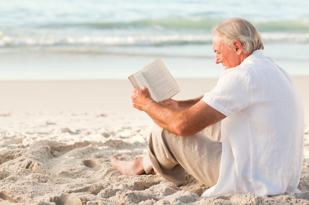 Mens die een boek op het strand leest