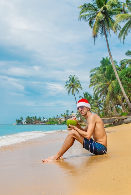 Mens die een cocktail met Kerstmanhoed drinkt op het strand