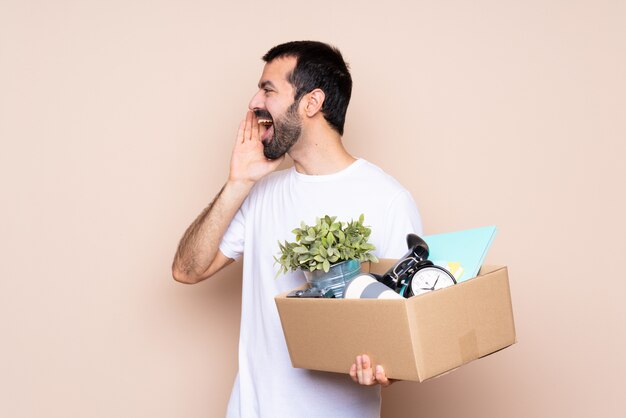 Mens die een doos houdt en zich in nieuw huis over geïsoleerde muur beweegt die met mond wijd open voor de zij schreeuwen