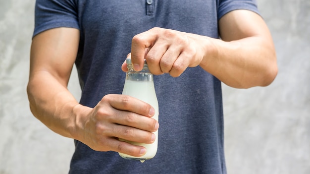 Mens die een fles melk op grijze achtergrond houdt.