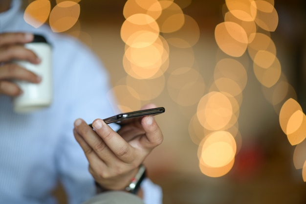 Mens die een mobiele telefoon op bokehlicht houdt in nacht atmosferische stad