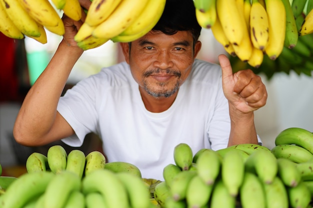Mens die gele bananen op lokale markt in Thailand verkoopt