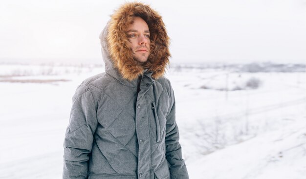 Mens die grijs de winterjasje met kap draagt in de wintersneeuw