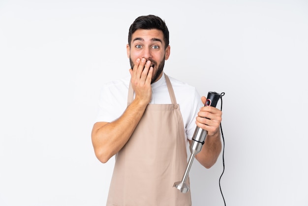 Mens die handmixer gebruikt die op witte muur met verrassingsgelaatsuitdrukking wordt geïsoleerd