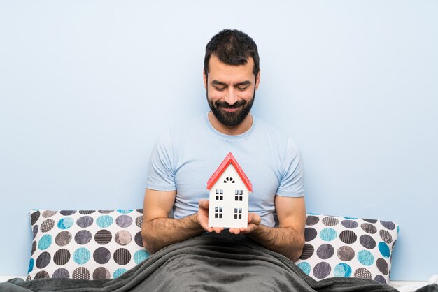 Mens die in bed met baard een klein huis houdt