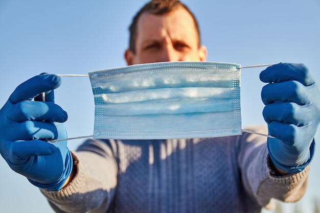 Foto mens die in blauwe beschermende handschoen medisch gezichtsmasker op zijn gezicht houdt