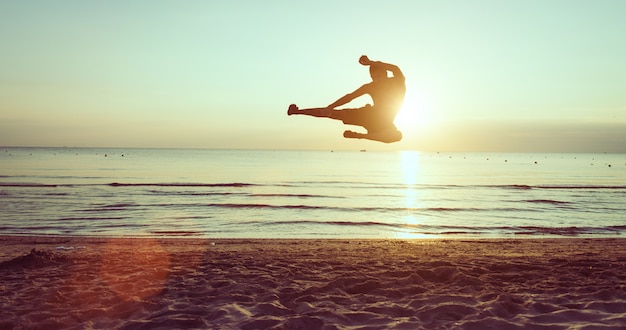 Mens die in een taekwondobeweging springen op het strand