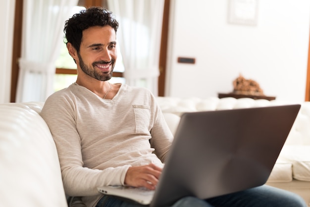 Mens die laptop met behulp van terwijl het zitten op de laag in zijn woonkamer