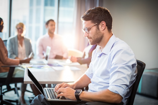 Mens die laptop met behulp van terwijl medewerker die op de achtergrond op elkaar inwerken