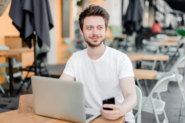 Mens die laptop voor het verre werk in koffie met behulp van