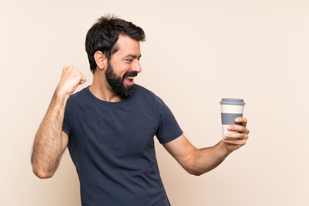 Mens die met baard een koffie houdt die een overwinning viert