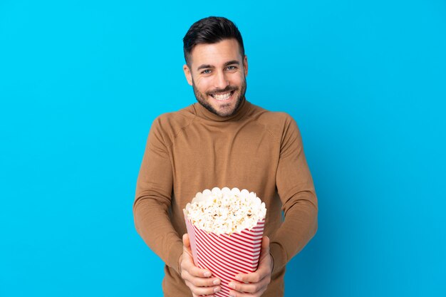 Mens die met baard popcorns over geïsoleerde muur houden