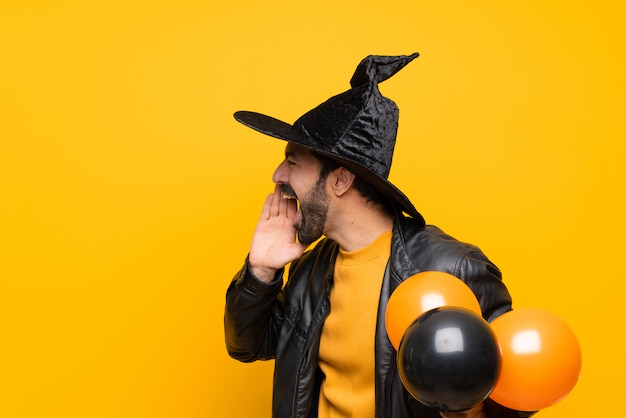 Mens die met heksenhoed zwarte en oranje luchtballons houden voor Halloween-partij die met mond wijd open voor de zij schreeuwen