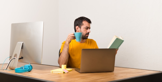 Mens die met laptot in een bureau werkt dat een boek leest