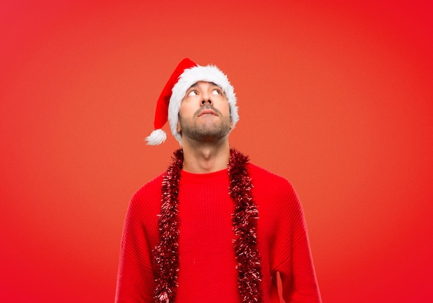 Mens die met rode kleren de Kerstmisvakantie viert die omhoog met ernstig gezicht kijkt