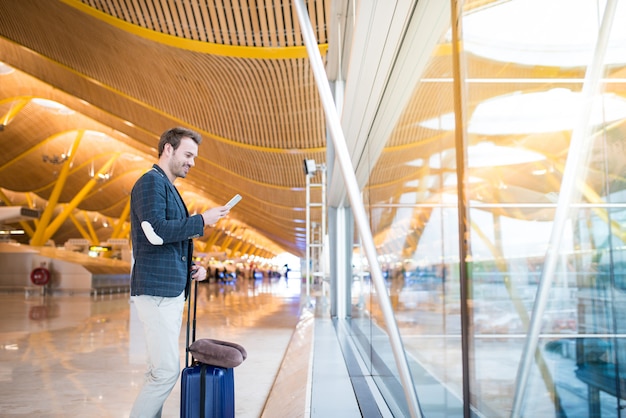 Mens die mobiele telefoon met behulp van bij de luchthaven die door het venster kijken