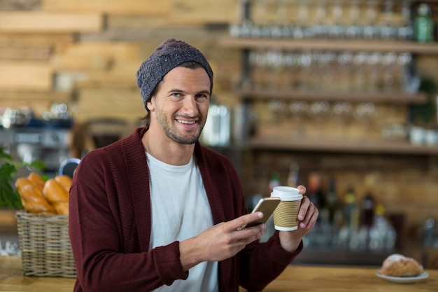 Mens die mobiele telefoon met behulp van terwijl het hebben van een koffie bij teller in koffie