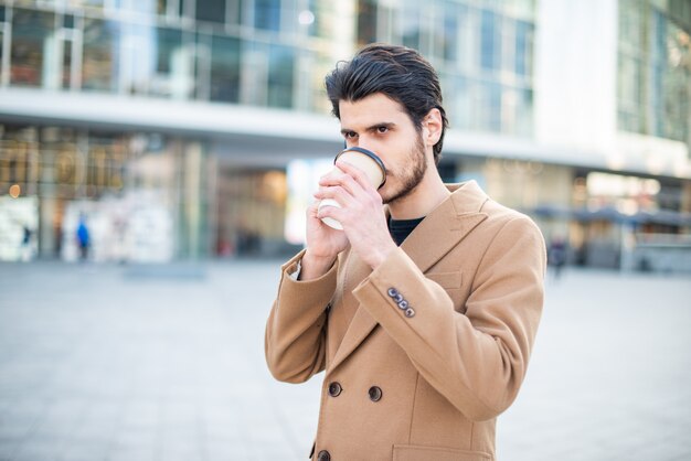 Mens die op de telefoon spreekt en een kop van koffie houdt terwijl het lopen in een stad