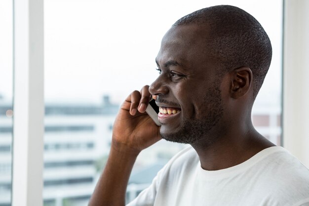 Mens die op mobiele telefoon dichtbij venster thuis spreekt