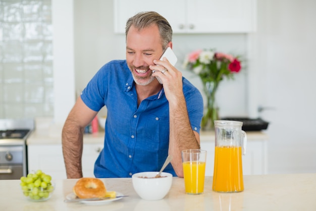 Mens die op mobiele telefoon spreekt terwijl het hebben van ontbijt in keuken