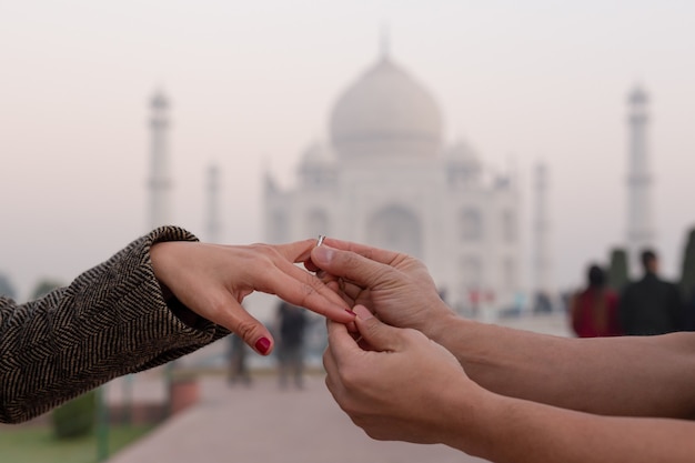 Mens die op verlovingsring op zijn vrouwenvinger zet met mahal Taj op achtergrond.