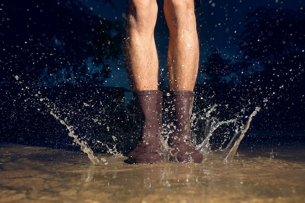 Mens die regenlaarzen draagt ​​die in een vulklei springen. Detailopname