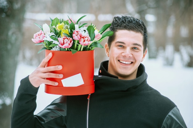 Mens die rode giftdoos met mooi boeket van bloeiende roze, gele en witte tulpen en witte chrysanten met groene bladeren houden, in openlucht