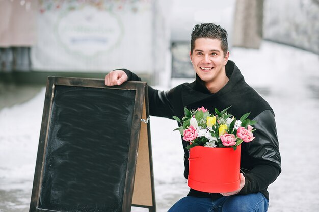 Mens die rode giftdoos met mooi boeket van bloeiende roze, gele en witte tulpen en witte chrysanten met groene bladeren houden, in openlucht