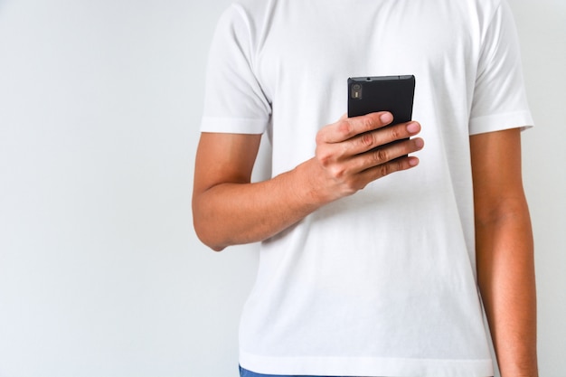 Foto mens die witte t-shirt draagt die en zwarte smartphone op witte achtergrond houdt gebruikt