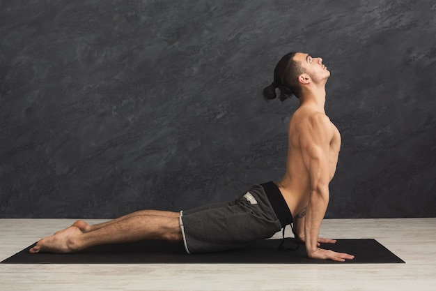 Mens die yoga doet. sportman doet cobra-houding, strekt zich uit op mat op grijze achtergrond, kopieer ruimte