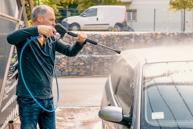 Mens die zijn auto met het gebruiken van een straal van het hoge drukwater wast