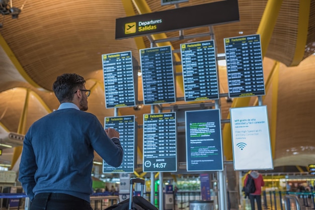 Mens die zijn vlucht controleert op de tijdschemavertoning bij de luchthaven