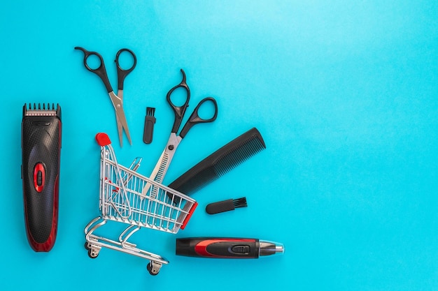 Mens haircut machine scissors and comb lie in a mini cart on a blue background