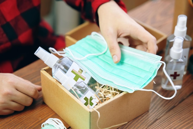 Mens hands put medical masks in a gift box with alcohol antiseptics sticker with a red cross on the ...