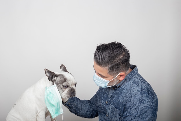 Mens in beschermend chirurgisch masker en latexhandschoenen die zijn huisdier strijken. Franse bulldog hond