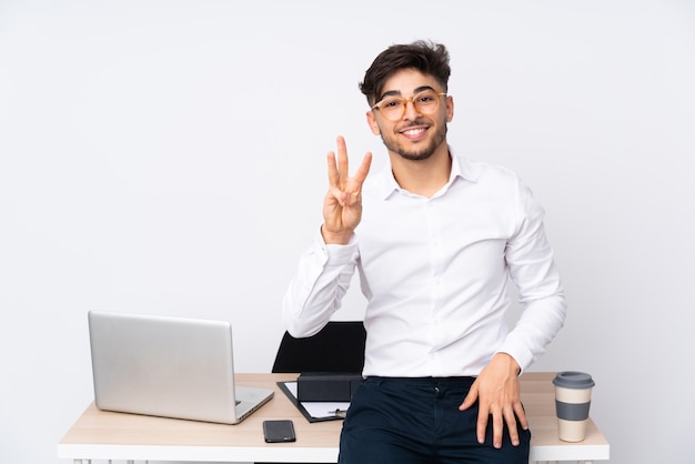 Mens in een bureau dat op witte gelukkige muur wordt geïsoleerd en drie met vingers telt