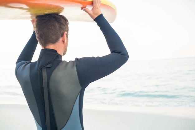 Mens in wetsuit met een surfplank op een zonnige dag