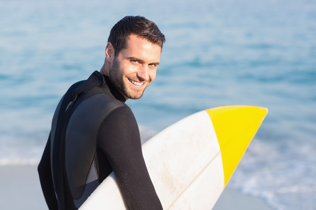 Mens in wetsuit met een surfplank op een zonnige dag