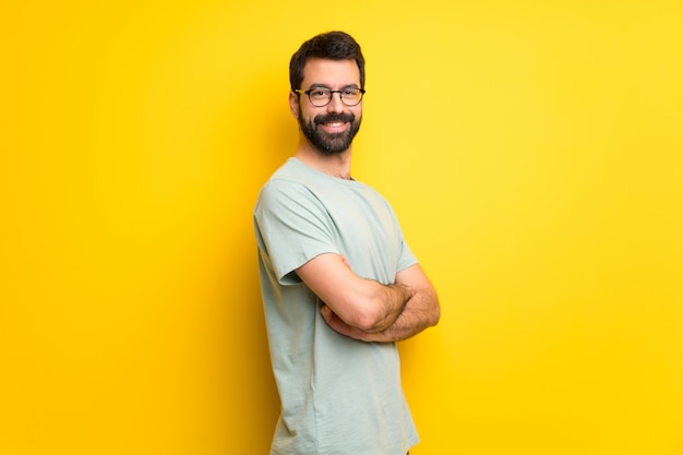 Mens met baard en groen overhemd die de wapens houden die in zijpositie worden gekruist terwijl het glimlachen