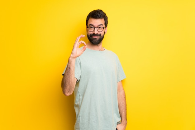 Mens met baard en groen overhemd die een ok teken met vingers tonen