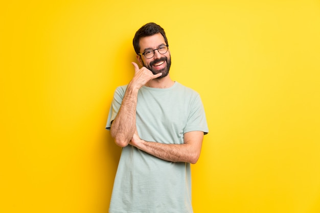 Mens met baard en groen overhemd die telefoongebaar maken. Bel me terug teken